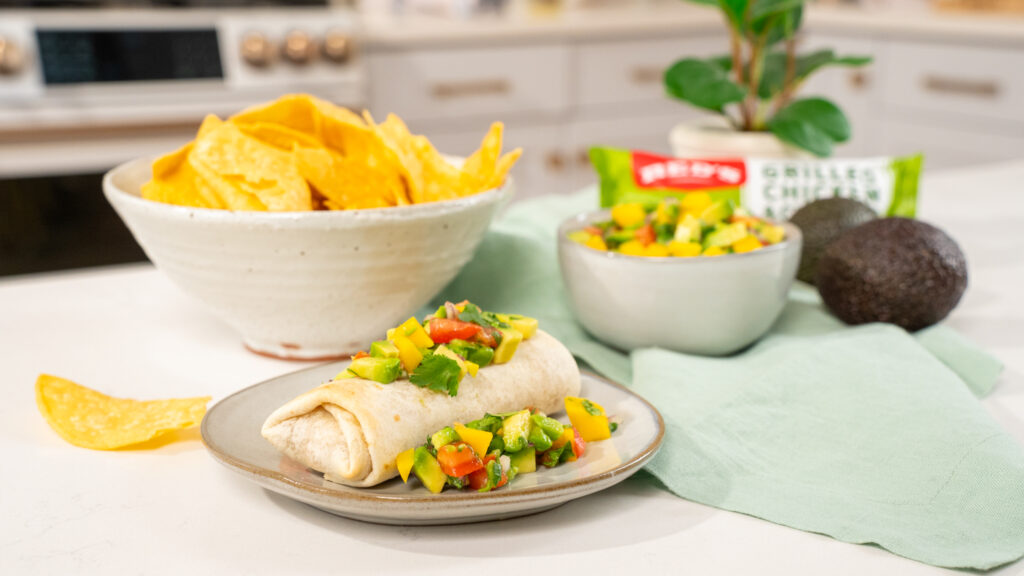 Brand marketing photo of a studio kitchen scene featuring a burrito topped with vibrant mango and avocado salsa. Tortilla chips in the background add to the appetizing display. The setup showcases our expertise in food videography and photography for colorful and fresh meal promotions.