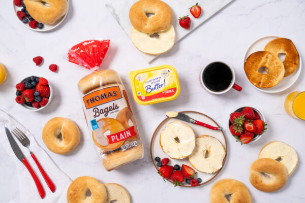 Breakfast scene featuring bagels with butter spread, fresh fruit, and coffee. Pops of red color from strawberries and silverware add vibrancy to the table setup. The appetizing display is perfect for a cozy morning meal.