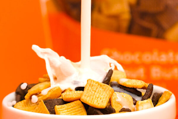 Action shot of milk being poured into cereal with the product being featured in the background.