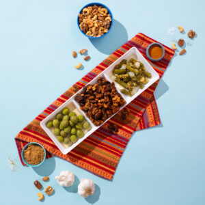 Spiced nuts in a tray with other appetizers like olives and cornichons. Food styled to perfection with contrasting colors and spills of seasonings.