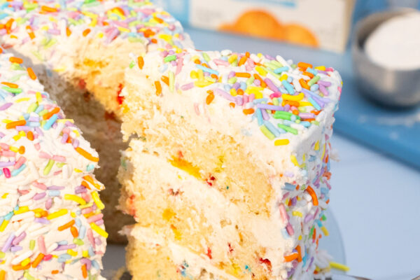 Sprinkle Smash Cake Lovely layered cake slice with sprinkles being pulled out to be plated with featured product in the background.