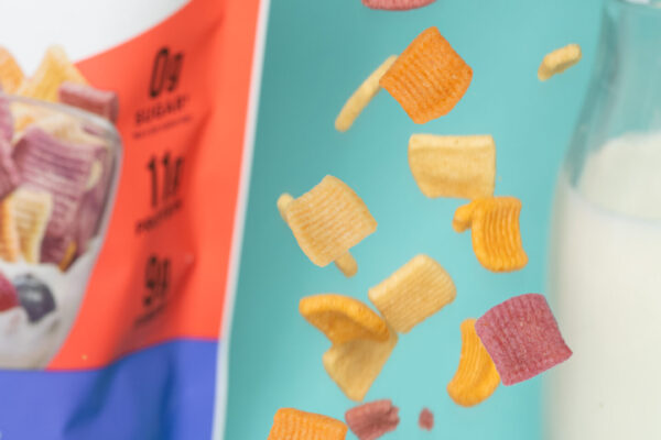 Close-up of cereal pouring into a bowl on a vibrant blue background, with a carefully styled backdrop of milk cascading in motion. Perfect for showcasing the dynamic appeal of breakfast cereals in marketing campaigns.