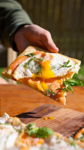 Eggs benedict pizza with hand pulling the slice up and a delicious egg oozing out. All in natural lighting.