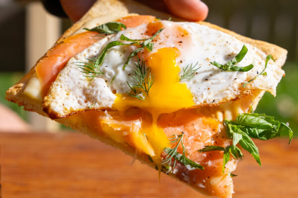 BenedictPizza07644 Eggs benedict pizza with hand pulling the slice up and a delicious egg oozing out. All in natural lighting.