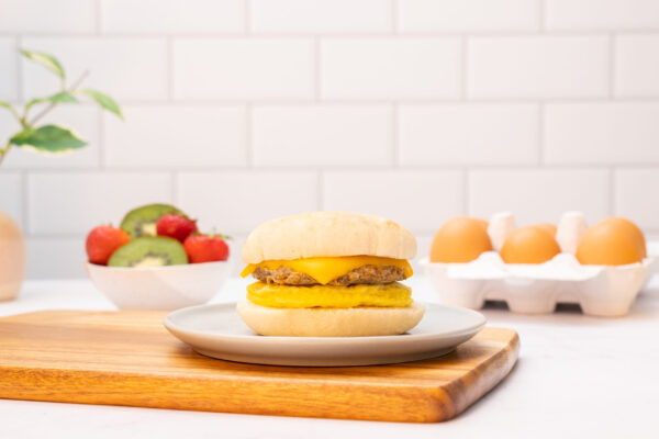 Breakfast Sandwich Breakfast sandwich displayed on a wooden cutting board in a studio kitchen with white tile background.