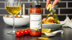 Pasta sauce featured in front of a pasta dish with a glass of wine. Food styling featured on a studio set with black brick and black marble.