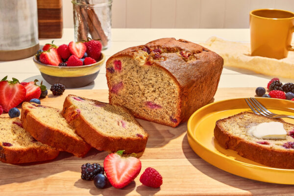 Berry Banana Bread Berry-studded banana bread showcased on a wooden cutting board, surrounded by fresh berries in the background, emphasizing its appeal for food brand marketing.