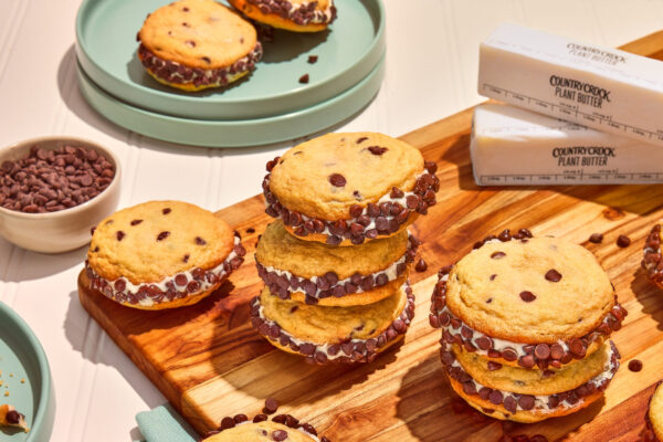 Chocolate Chip Cookie Sandwiches Stacked chocolate chip cookies with creamy frosting sandwiched between layers, artfully arranged on a rustic wooden cutting board. Captured to highlight the irresistible appeal and artisanal presentation.