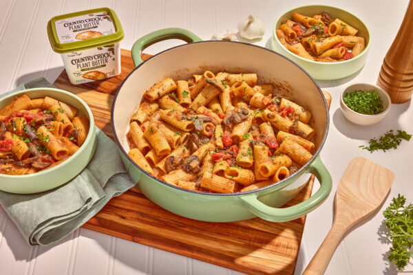 Mushroom Pasta Bake Presentation of a delectable mushroom pasta bake, artfully prepared in a vibrant green Dutch oven, resting on a textured wooden cutting board. The dish showcases hearty mushrooms, and a creamy sauce, highlighting its rustic appeal and comforting flavors.