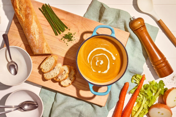 Creamy Vegetable Soup Rich and creamy vegetable soup captured in a rustic blue Dutch oven, elegantly presented on a wooden cutting board. Ideal for food CPG brands looking to showcase comforting and wholesome culinary creations in their marketing campaigns.