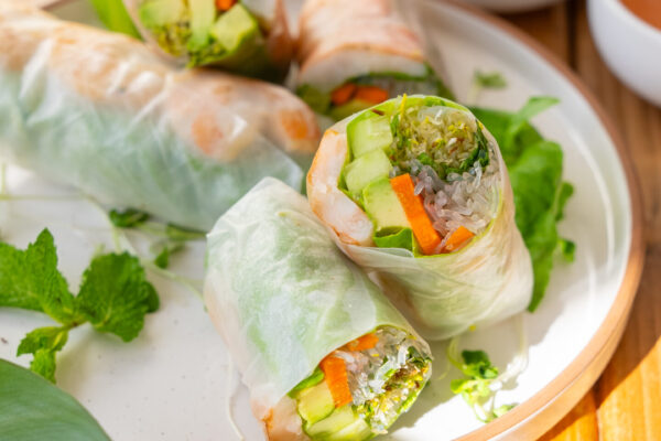 Fresh Shrimp Spring Rolls Freshly prepared spring rolls artfully arranged on a white plate, garnished with herbs, set on a rustic wooden table, highlighting the product's appeal for food brand marketing.
