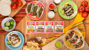 Taco seasonings centered in the frame with tacos and assorted toppings arranged on a rustic wooden surface, emphasizing their vibrant colors and savory appeal.