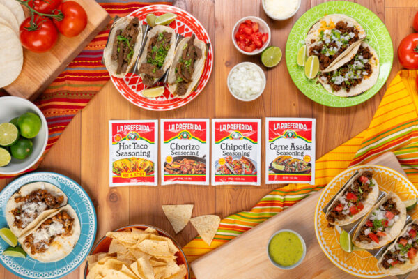 Taco Seasonings Taco seasonings centered in the frame with tacos and assorted toppings arranged on a rustic wooden surface, emphasizing their vibrant colors and savory appeal.