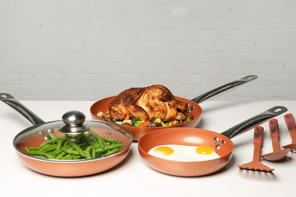 Copper Pan Set A crisp white setting showcasing a pan set with styled food, including a whole chicken, vegetables, and fried eggs, highlighting the freshness and culinary appeal of the ingredients.