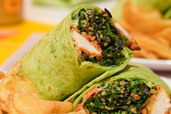 Chicken Salad Wrap Health-conscious chicken and kale wrap featuring a nutritious dressing product prominently displayed in the background, highlighting fresh ingredients and wellness appeal.