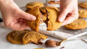 Food photography styled cookie with melted chocolate in the center and two hands pulling the cookie apart. Studio lighting and hand model on a marble counter.