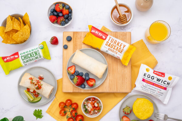 Burritos and Fresh Fruit Burritos artfully arranged on a marble surface with wooden cutting boards and fresh fruit, highlighting their savory appeal and gourmet presentation.