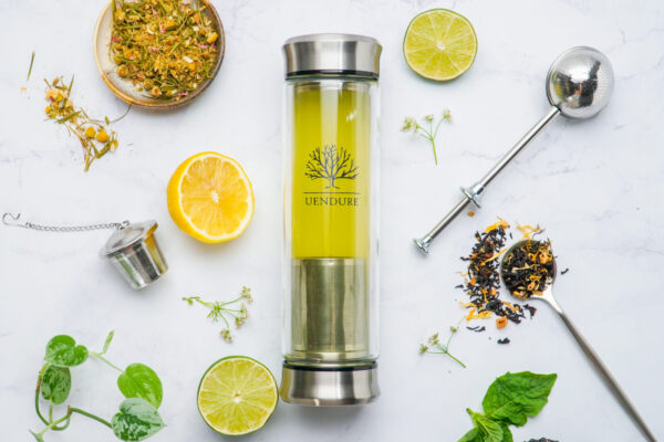 Tea Infuser with Fresh Ingredients Tea infuser bottle elegantly placed on a marble surface, showcasing featured tea and fresh ingredients in a tasteful composition.