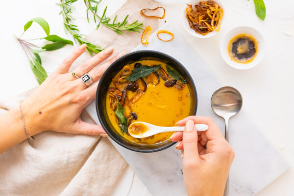 Squash soup topped with a drizzle of brown butter, crispy sage and sauteed mushrooms. On a styled set with natural lighting to create an enticing dish scene.